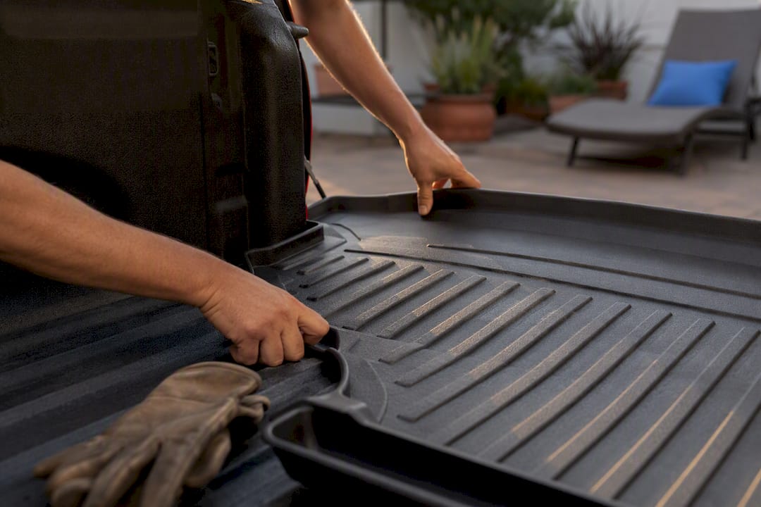 Hands fitting custom heavy rubber bed mat into truck bed