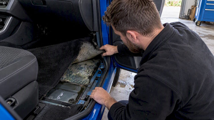 Lifted carpet reveals damp vehicle floor padding