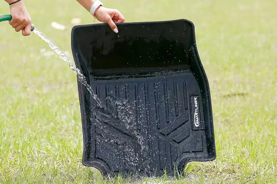 Person pouring water onto a black car mat on grass