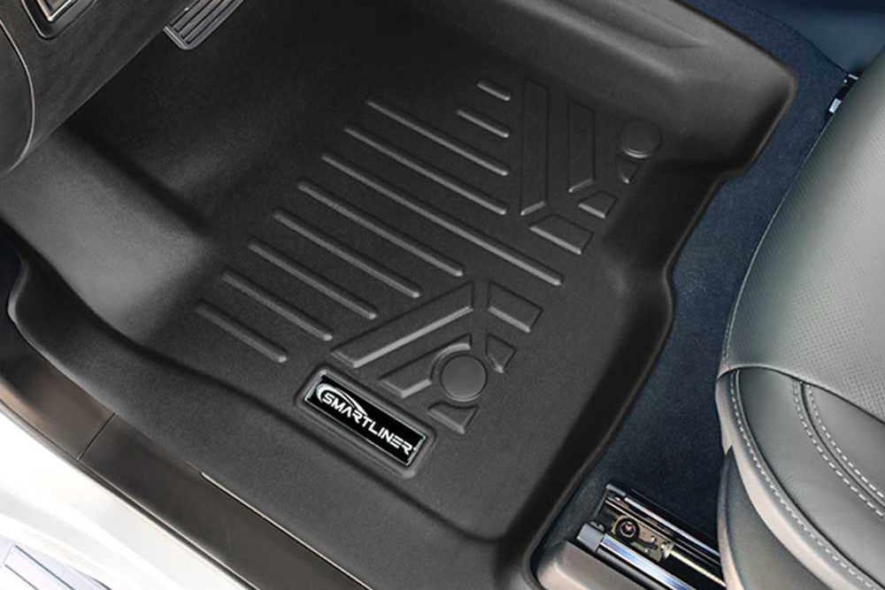 A black rubber car floor mat installed in a GMC Sierra 1500's footwell, shown from above. The mat has ribbed texture and a visible 'SMART LINER' brand patch near the bottom edge.